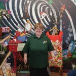 Picture of Anita stood at work with a colourful background behind her